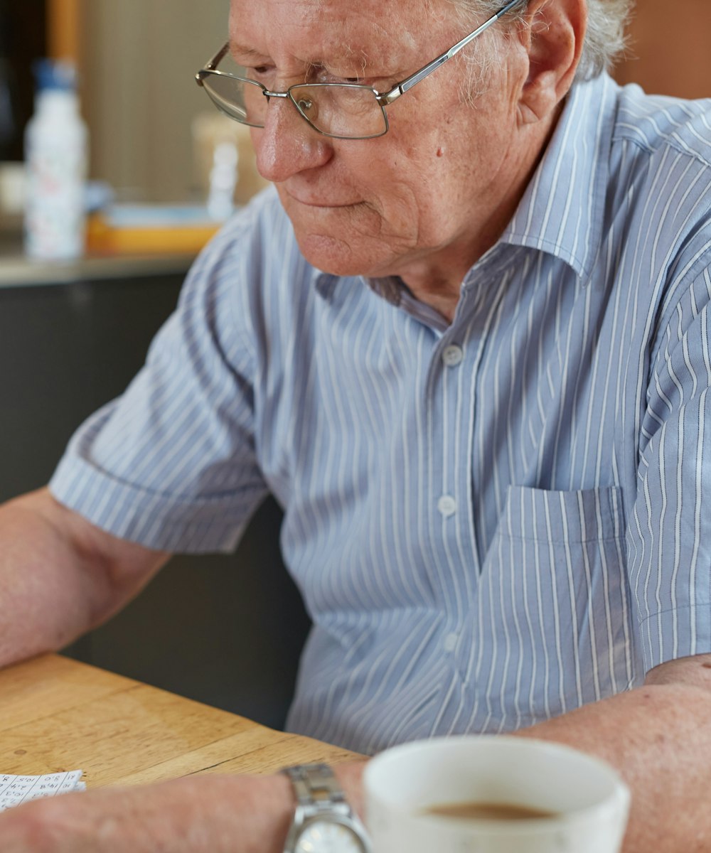 An older man at his kitchen table writing notes on a sheet of paper