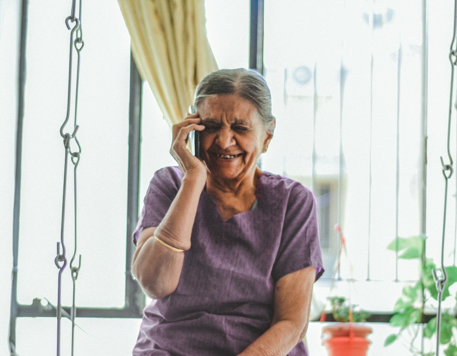 An older woman laughing on a phone call by the window