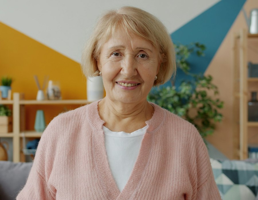 An older woman in a pink cardigan smiling at home